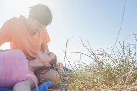 Couple sitting in grass, woman's head on man's lapの写真素材