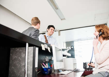 Two men at reception and woman on telephone
