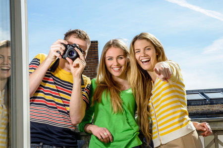 Three young friends with camera on rooftopの写真素材