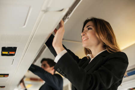 Air stewardess closing overhead locker on aeroplaneの写真素材
