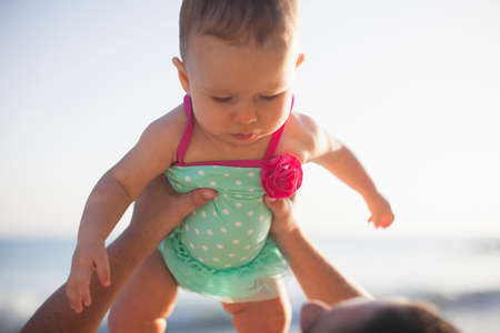 Woman lifting baby girl wearing swimsuitの写真素材