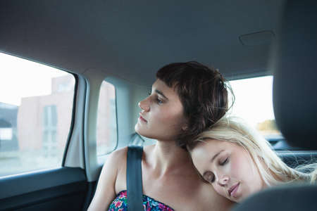 Women in backseat of car, one with head on friend's shoulderの写真素材