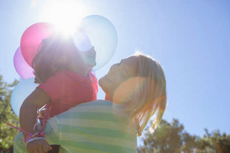 Mother hugging daughter in sunlight with basket of balloonsの写真素材