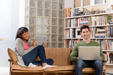 Young couple on sofa, man using laptop woman with digital tablet