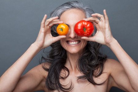Mature woman covering eyes with red and yellow tomatoの写真素材