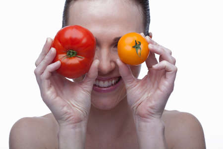 Young woman covering eyes with red and yellow tomatoの写真素材