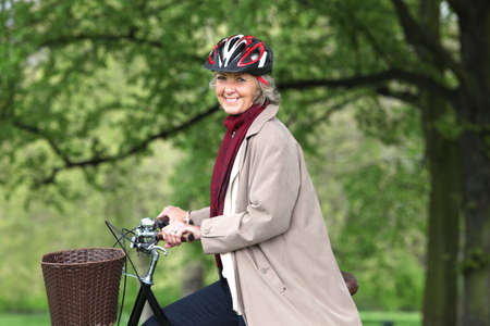 Senior woman riding bicycle in park, portraitの写真素材