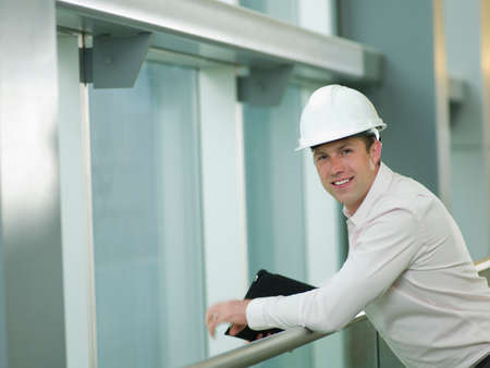 Mid adult construction worker in hard hat leaning on railing, portrait