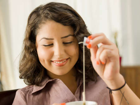 Young woman lifting teabag from cup, smiling