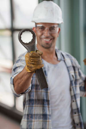 Mid adult construction worker wearing hard hat and holding wrench, portrait