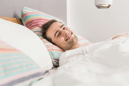 Mid adult man lying in bed under duvet
