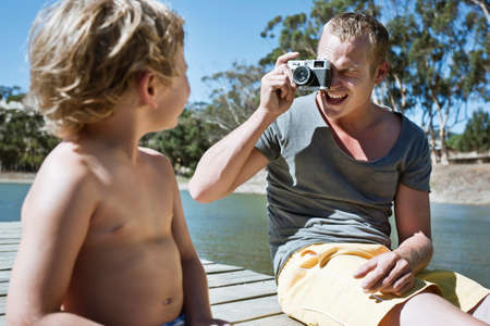 Man taking photo of boy sitting on jetty