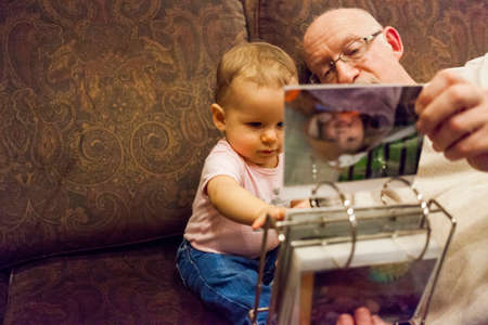 Grandfather and baby granddaughter looking at photo albumの写真素材