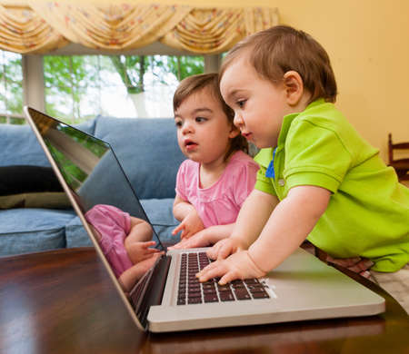 Two young toddlers playing with laptopの写真素材