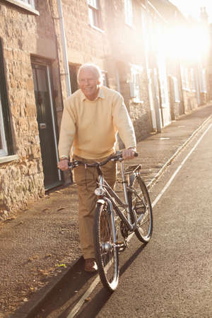 Senior man pushing his bicycle on streetの写真素材
