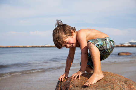 Boy crouching on rock on beachの写真素材