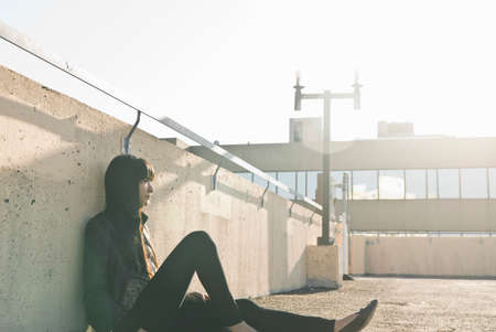 Young woman sitting on sunlit rooftop