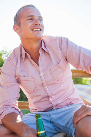 Young man holding bottle and smiling in sunlightの写真素材