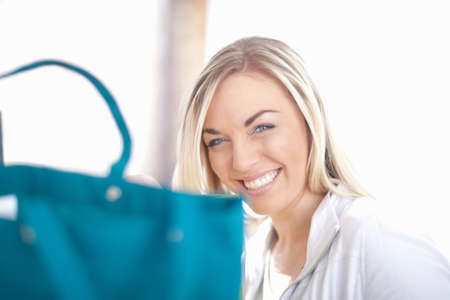 Young woman sitting behind turquoise shopping bagの写真素材