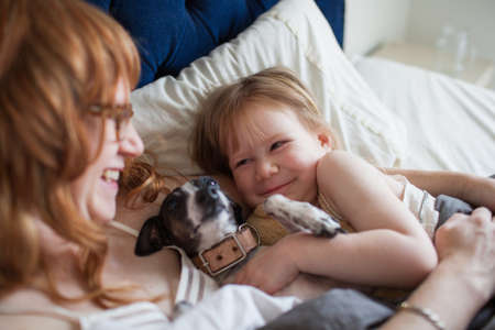 Mother, daughter and dog lying in bedの写真素材