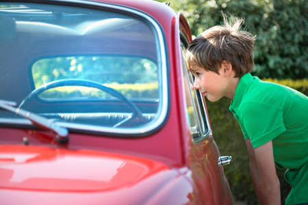 Boy looking through window of vintage automobileの写真素材
