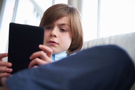 Boy on sofa using digital tabletの写真素材
