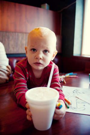 Young boy reaching for milkshake in cafeの写真素材