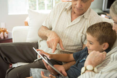 Grandparents sitting with grandson and looking at digital tabletの写真素材