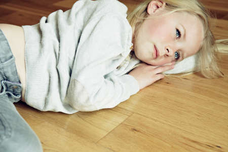 Young girl lying on wooden floor, looking awayの写真素材