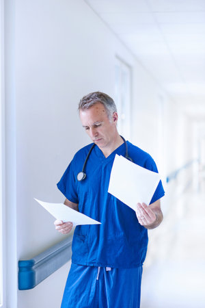 Doctor standing in corridor reading medical recordsの写真素材