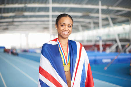 Young female athlete wrapped in UK flag with gold medalの写真素材