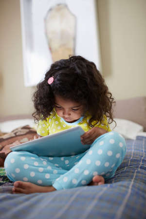 Child sitting on bed using digital tabletの写真素材