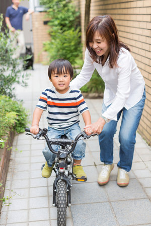 Mother helping son to ride a bikeの写真素材
