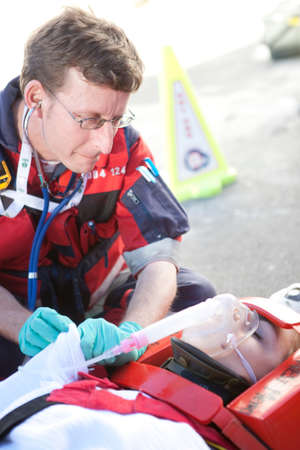 Paramedic using stethoscope, patient on stretcher wearing oxygen maskの写真素材