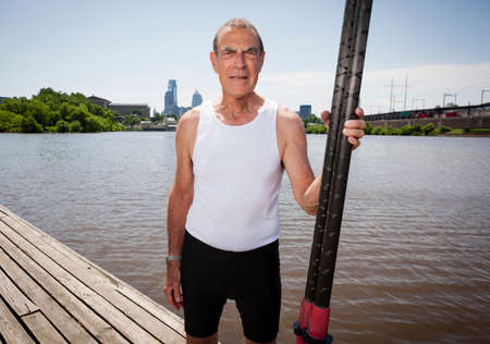 Senior man on pier holding oars