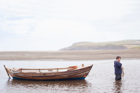 Man pulling rowing boat through water, Wales, UKの写真素材