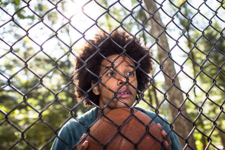 Portrait of young man holding basketball through wire fenceの写真素材