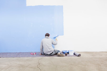 Rear view of man painting wall blueの写真素材