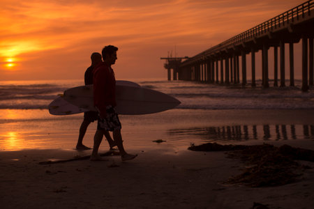 Two men carrying surfboards on beachの写真素材