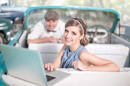 Man watching woman use laptop in back seat of convertible