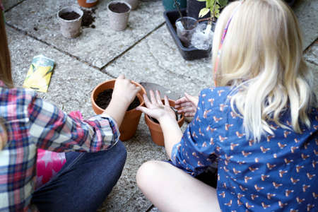 Close up of two girls in garden planting seeds into potsの写真素材