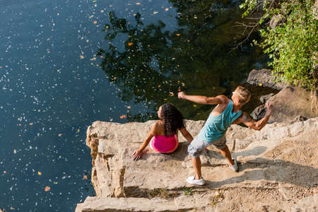 Young couple throwing stones from rock ledge, Hamburg, Pennsylvania, USAの写真素材