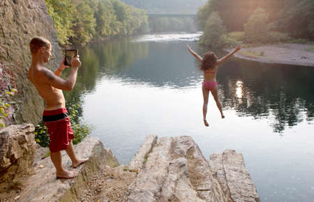 Young couple photographing jump from rock ledge, Hamburg, Pennsylvania, USAの写真素材