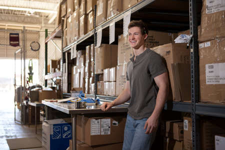 Worker standing in warehouse, leaning against shelving