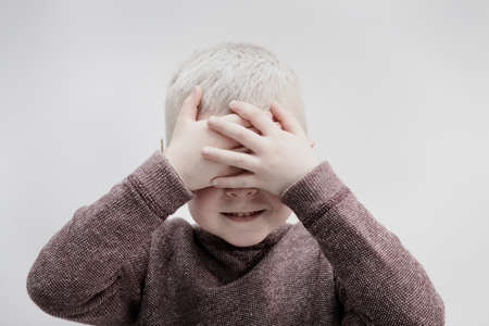 Portrait of boy wearing brown jumper, covering face with handsの写真素材