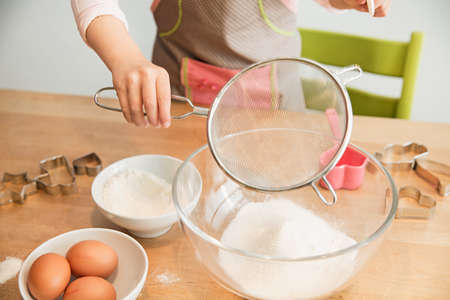 Girl sieving flour into mixing bowlの写真素材