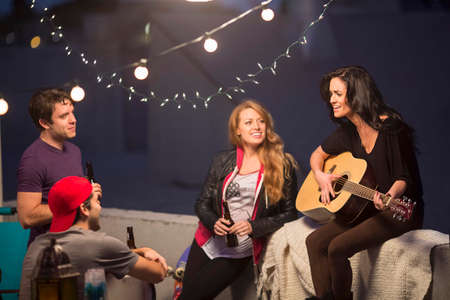 Young adult friends listening to guitar at partyの写真素材