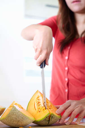 Young woman in kitchen slicing melonの写真素材