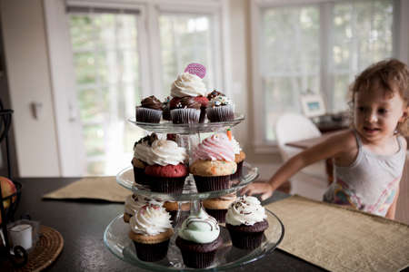 Female toddler looking at cake stand full of cupcakes