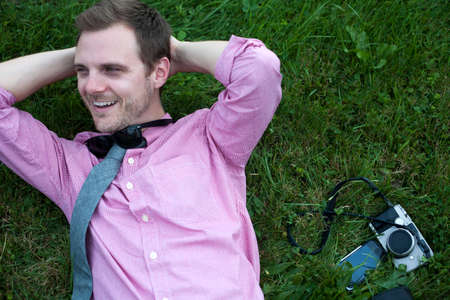 Mid adult man with camera and smartphone relaxing on grassの写真素材